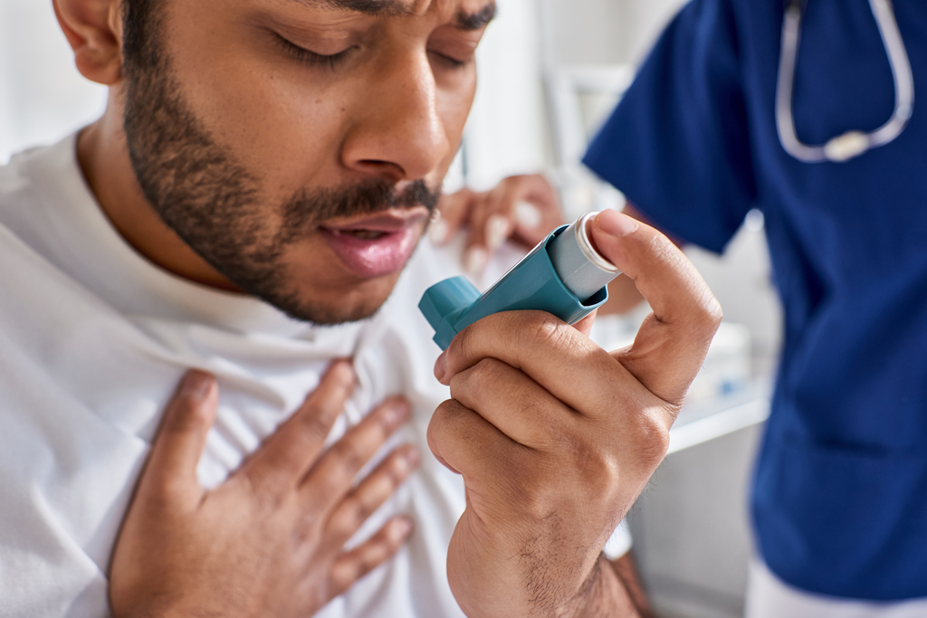 african american nurse helping her indian patient with asthma inhaler in his hospital ward
